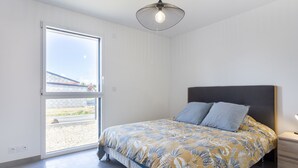 A bedroom with a bed, a nightstand, a modern pendant light, and a large window.