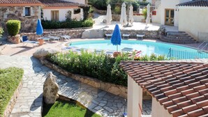 A pool area with lounge chairs and umbrellas, surrounded by stone buildings with tiled roofs.