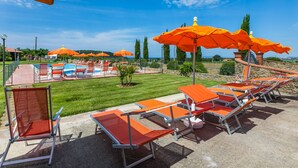A poolside area with lounge chairs and umbrellas, a pool, and a clear sky.