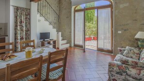 Ein geräumiger Wohnbereich mit einer Holztreppe, einem mit Gebäck gedeckten Esstisch und einem Sofa mit floralem Bezug.