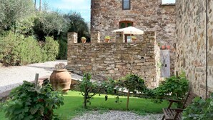 Un bâtiment en pierre doté d’un petit balcon, d’un grand pot de fleurs et d’un banc, le tout situé dans un jardin.
