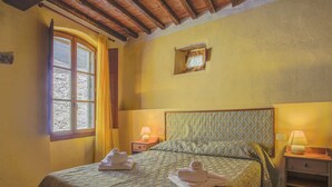 Une chambre à coucher avec un lit, deux tables de chevet, une fenêtre avec des rideaux, un plafond en bois et un petit cadre photo accroché au mur.