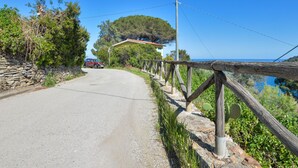 A narrow road with a stone wall on one side and a wooden fence on the other, leading to a house with a red roof. - Baroccia da Mary by Interhome (Rio Marina)