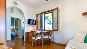 A dining area with a wooden table and chairs, a television mounted above it, and a window with a view of greenery. - Baroccia da Mary by Interhome (Rio Marina)