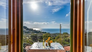 Ein Balkon mit Tisch für zwei Personen, mit Blick auf eine Küstenlandschaft mit Hügeln und blauem Himmel.
