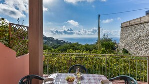 A balcony with a table set for two, overlooking a scenic landscape with a stone wall and lush greenery. - Apartment Giulia by Interhome (Capoliveri)