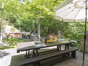 A picnic table set up in a lush garden with a pool and outdoor seating area in the background. - Cottage Contadina by Interhome (Cortona)