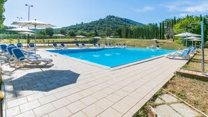 Une piscine entourée de chaises longues et de parasols, elle-même bordée d’un jardin aménagé et avec une colline en arrière-plan.
