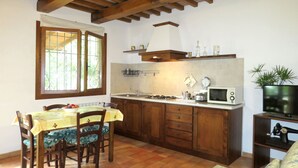 Une cuisine de taille réduite avec des meubles en bois, une table à manger avec des chaises, une fenêtre donnant sur un beau paysage et un téléviseur posé sur un meuble.