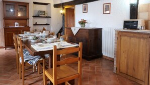 A dining area with a wooden table set for four, surrounded by chairs. There is a kitchen area with a stove, oven, and a small refrigerator. - Rosa - Borgo la Civitella by Interhome (Roccastrada)