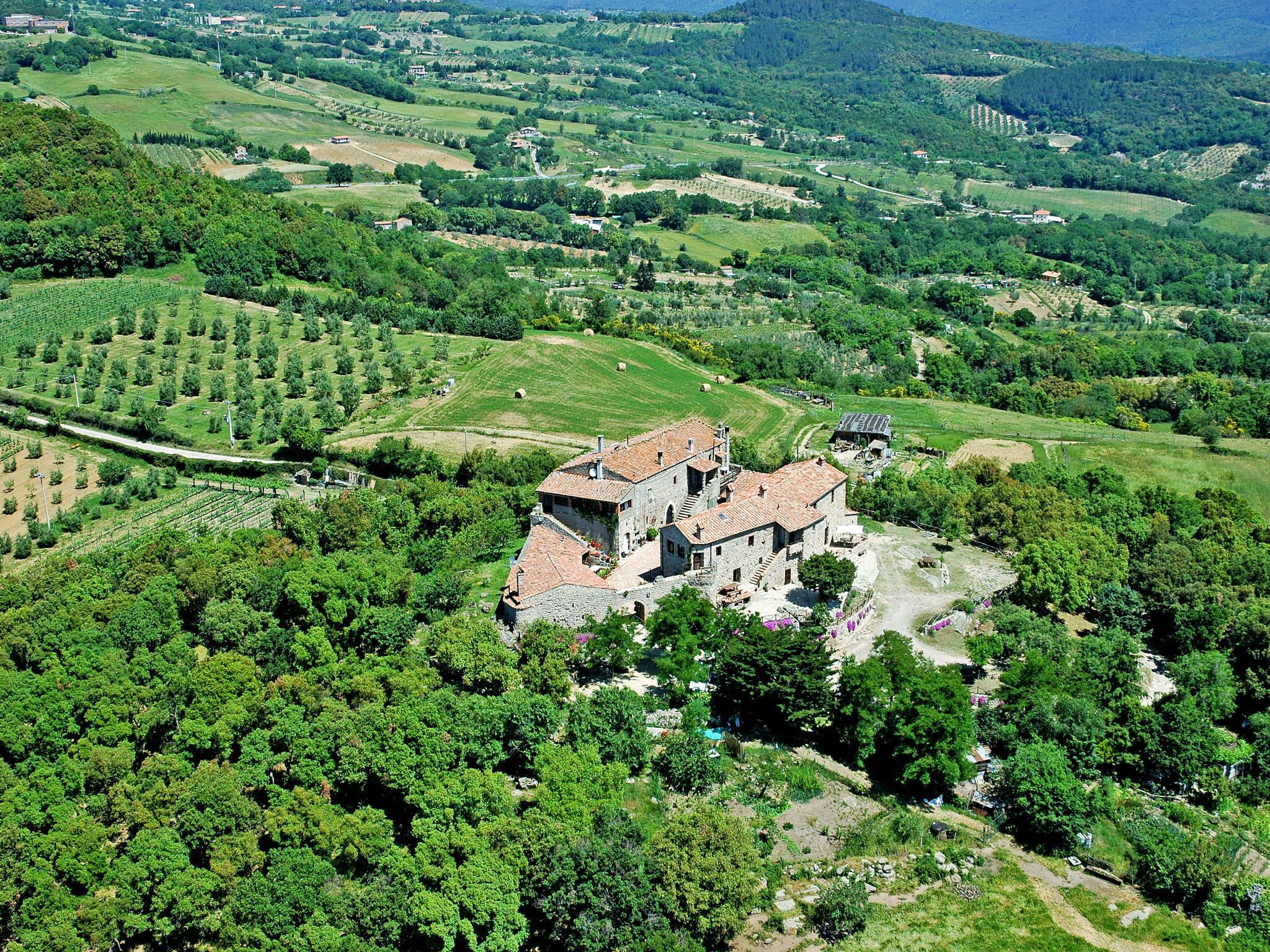 An aerial view of a rural area with a stone building surrounded by lush greenery and fields.
