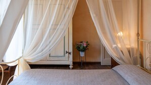 Un dormitorio con cama, cortinas blancas, una mesita con planta en maceta y techo de madera.