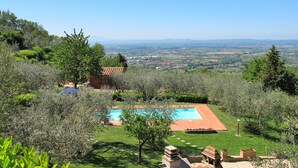 A pool surrounded by a garden with a view of the countryside.