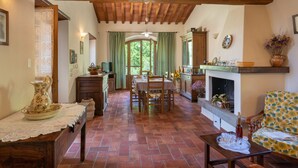 A cozy interior with a wooden ceiling, a dining area with a table and chairs, a fireplace, and a sofa with a floral pattern.