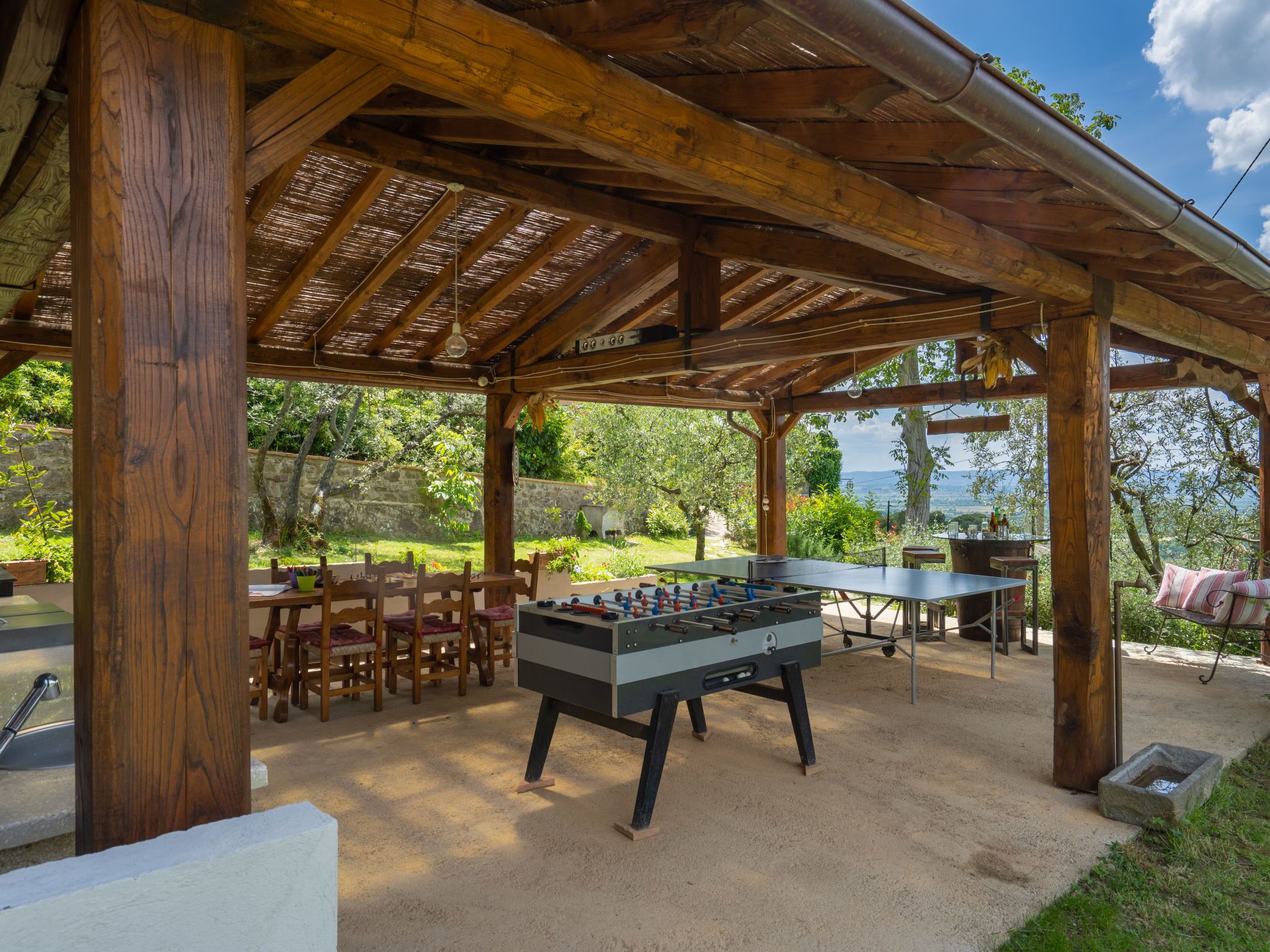 Une terrasse extérieure couverte, équipée d’une table de baby-foot, d’un espace salon et offrant une vue sur le paysage.