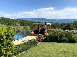 Un espace piscine agrémenté d’une pergola et de sièges, entouré d’une végétation luxuriante et offrant une vue sur les montagnes lointaines.