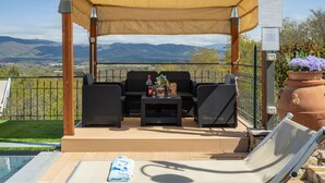 Een overdekt terras met rieten meubilair, een zwembad en uitzicht op de bergen.