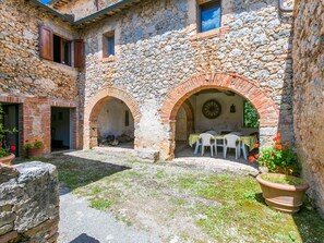 A courtyard with stone walls, a brick archway, and a table with chairs.