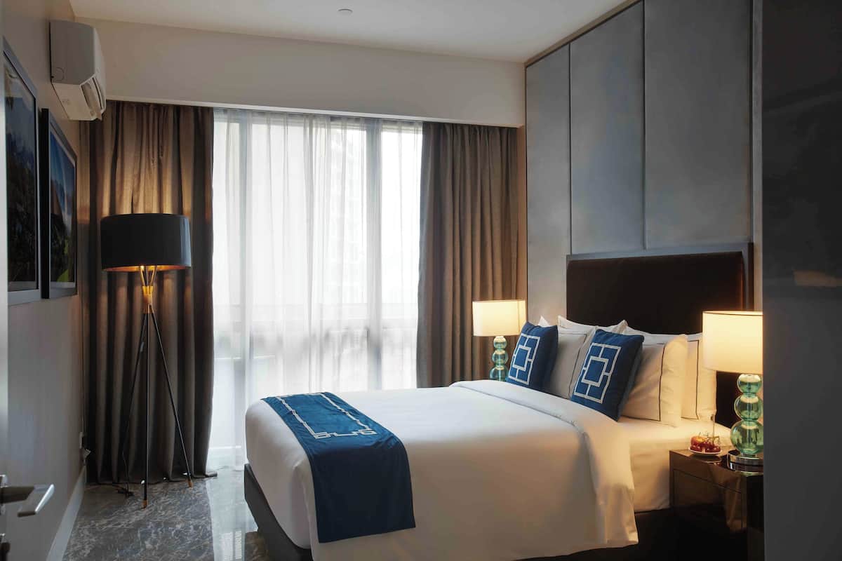 Ein Hotelzimmer mit einem großen Bett, zwei Nachttischlampen, einem Nachttisch und einem Fenster mit Vorhängen.