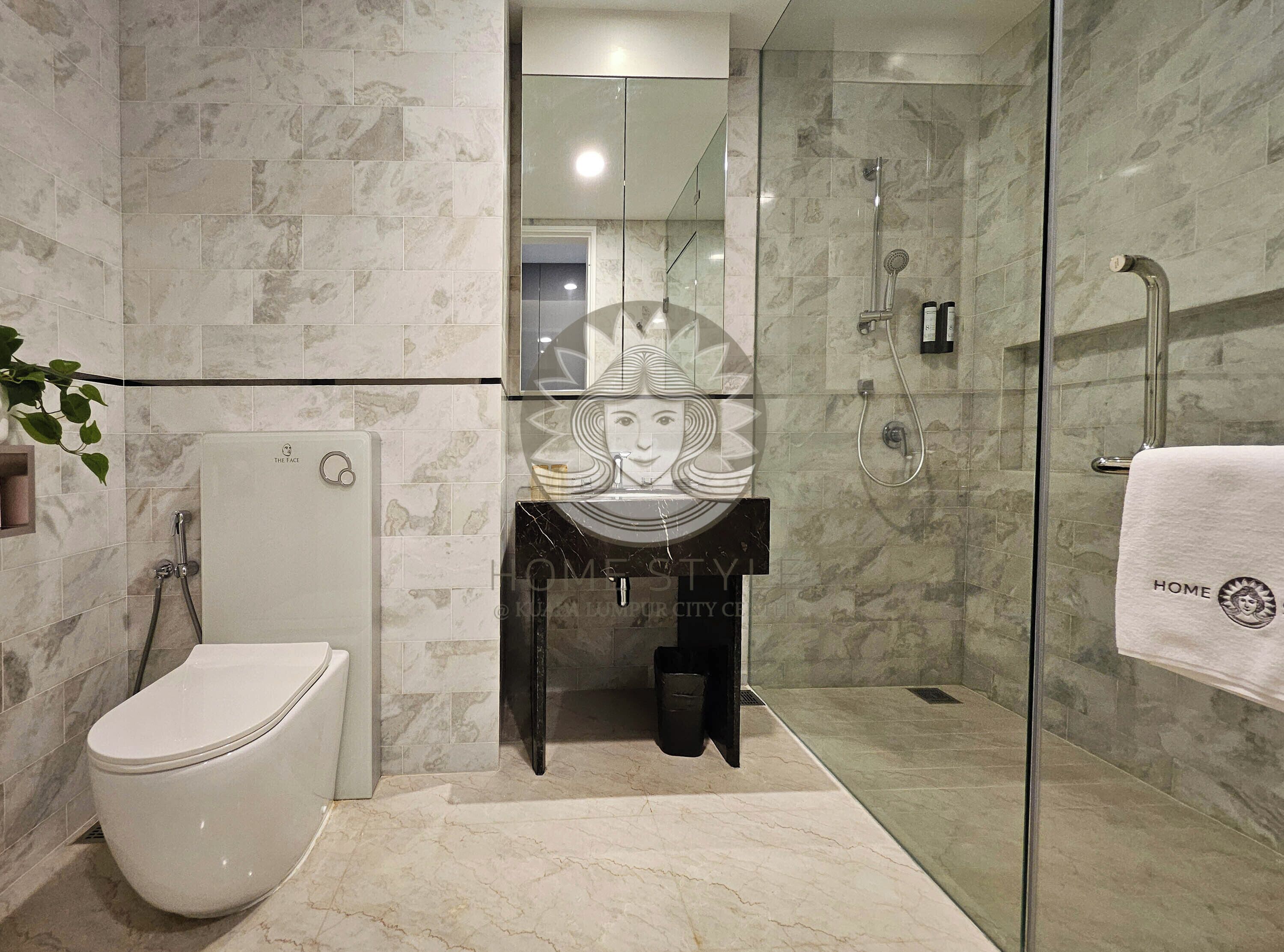 Ein modernes Badezimmer mit einer gläsernen Dusche, einer weißen Toilette und einem Waschbeckenbereich mit Marmorfliesen.