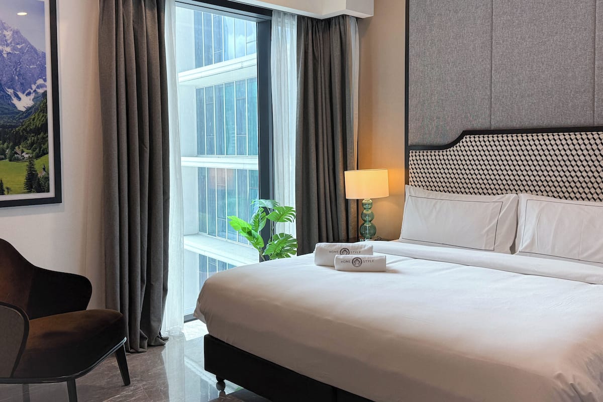Ein Hotelzimmer mit einem großen Bett, einem Nachttisch mit Lampe, einem gerahmten Bild an der Wand und einem Fenster mit Vorhängen.