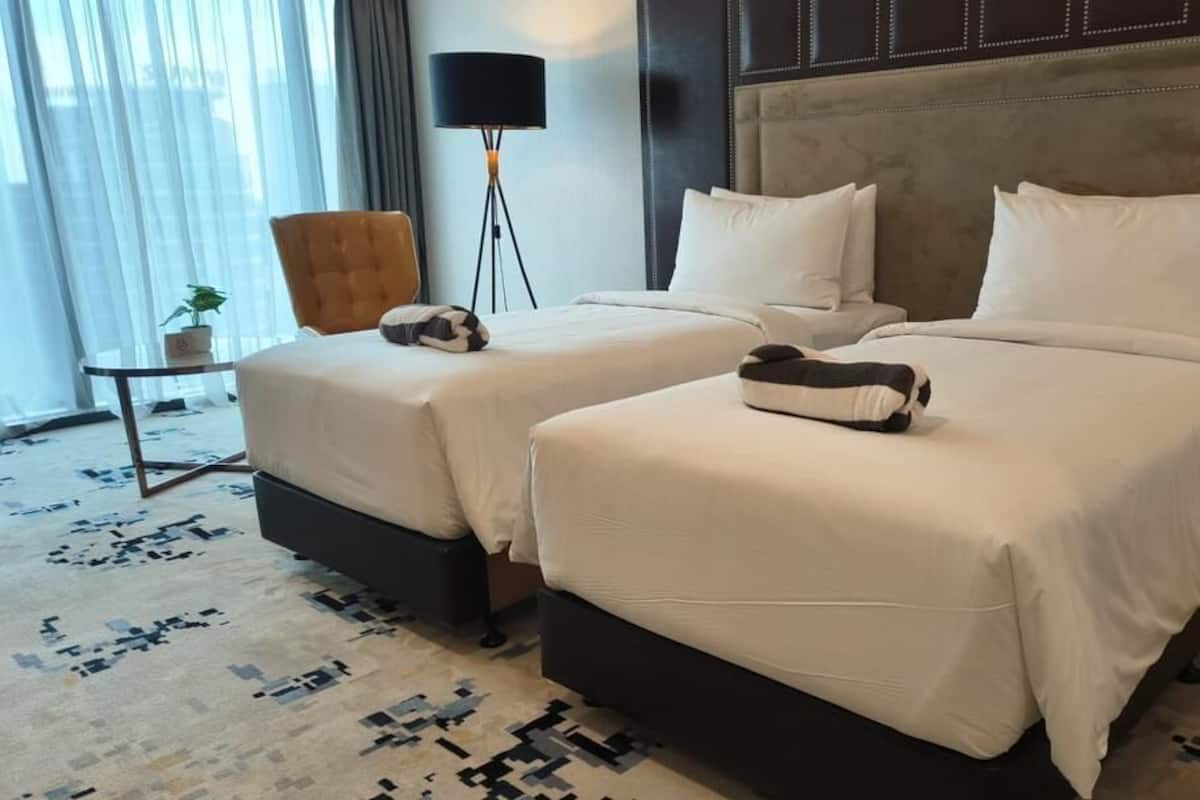 Ein Hotelzimmer mit zwei Betten, einem kleinen Tisch mit Lampe und einem Sessel.