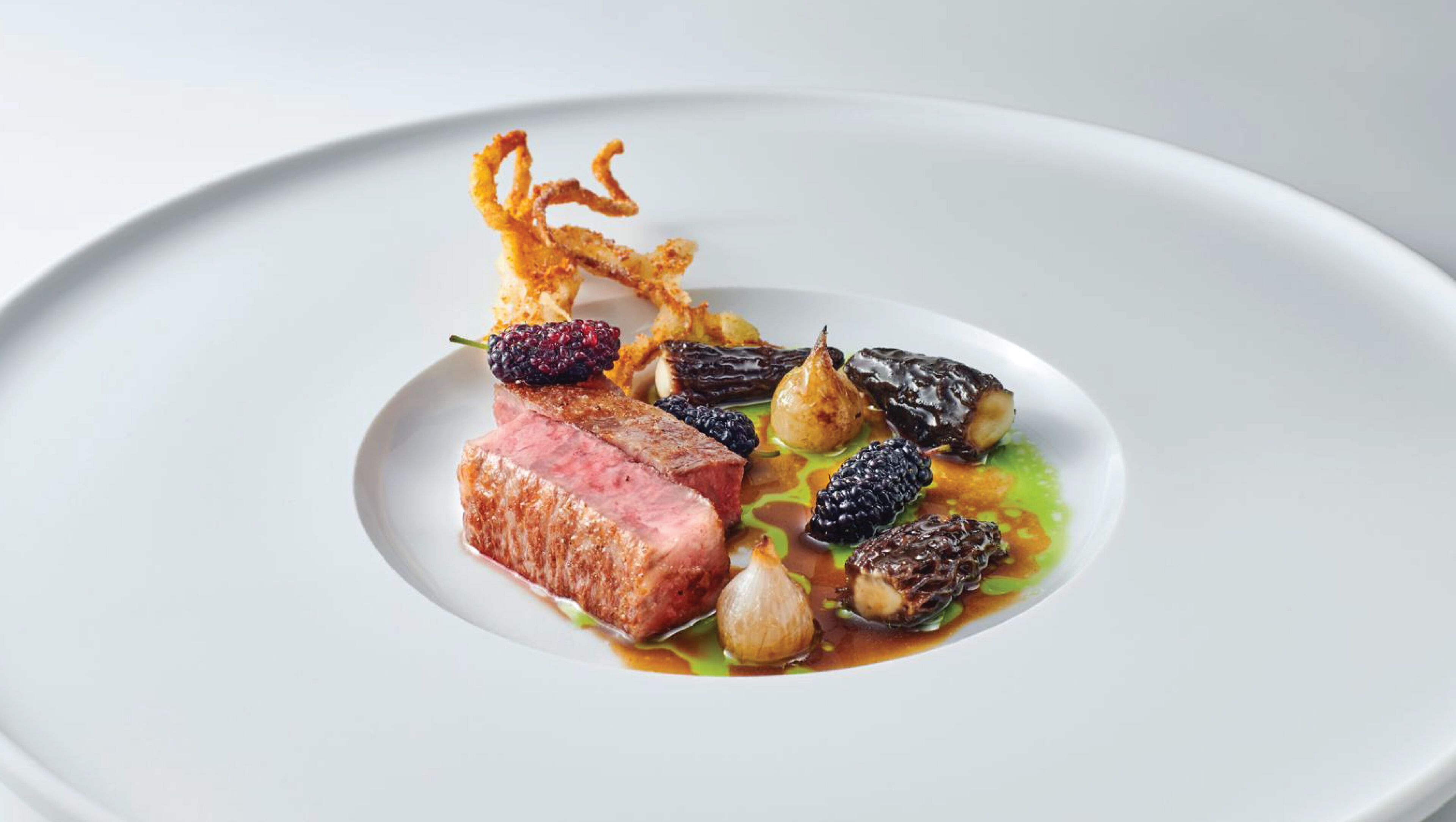 Une assiette blanche contenant un morceau de viande, des légumes et une sauce.