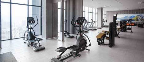 A modern gym with various cardio machines, large windows, and a cityscape view.