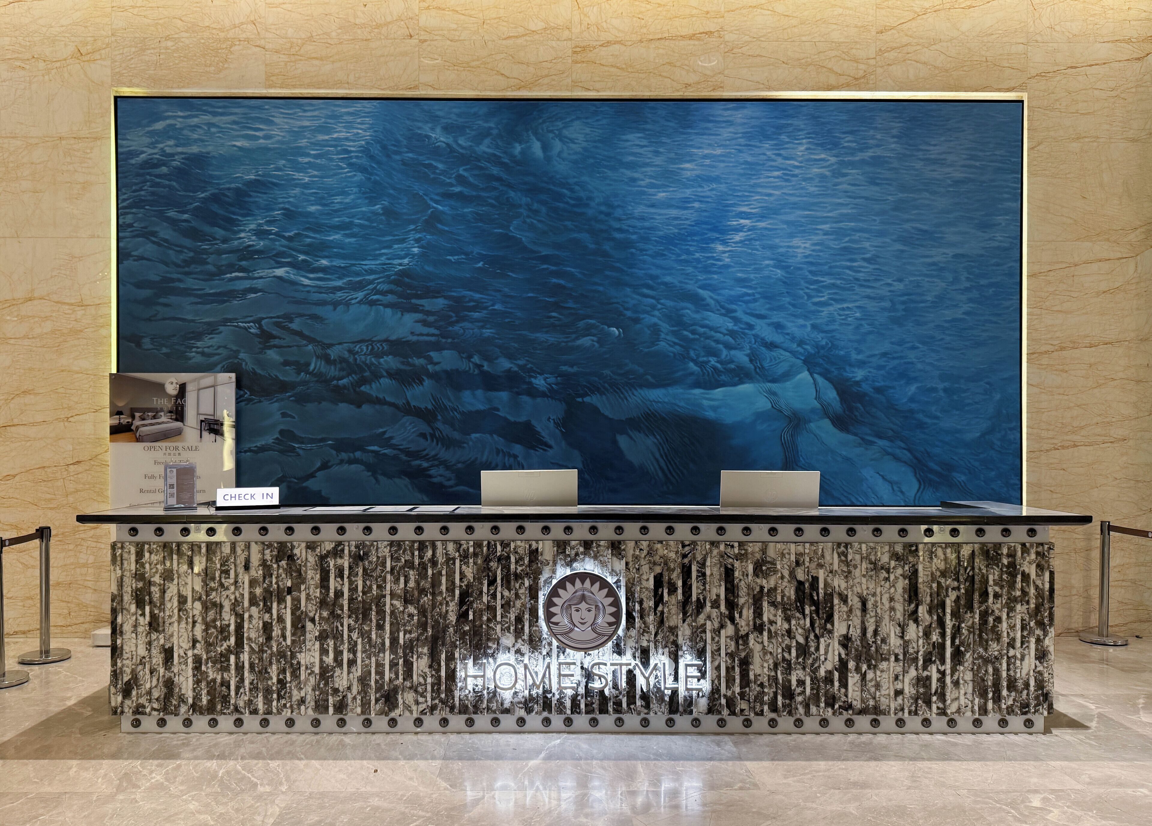 Una recepción con un gran monitor que muestra una escena submarina, un letrero que dice "HOMESTYLE" y un cartel de "CHECK IN".