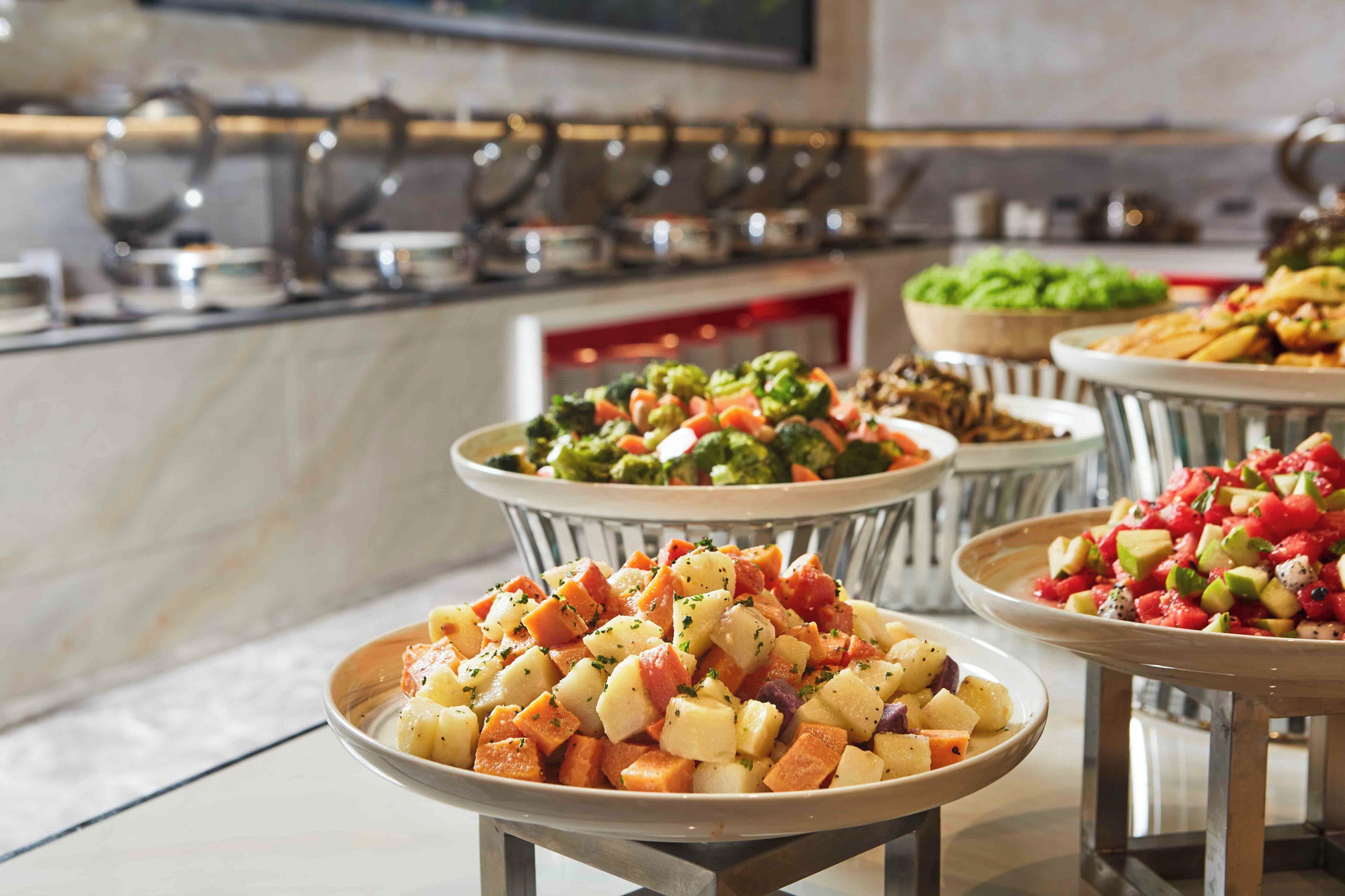Een buffet met diverse gerechten, waaronder een salade met gemengde groenten en een fruitsalade.