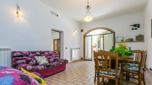 Une pièce spacieuse avec un canapé à motifs floraux, une table à manger avec des chaises, et une vue sur un espace extérieur accessible par un passage en arc de cercle.