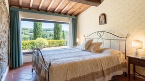 A bedroom with a bed, a nightstand, a window with curtains, and a view of greenery outside.