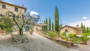A rustic courtyard with stone buildings, a gravel path, and potted plants.