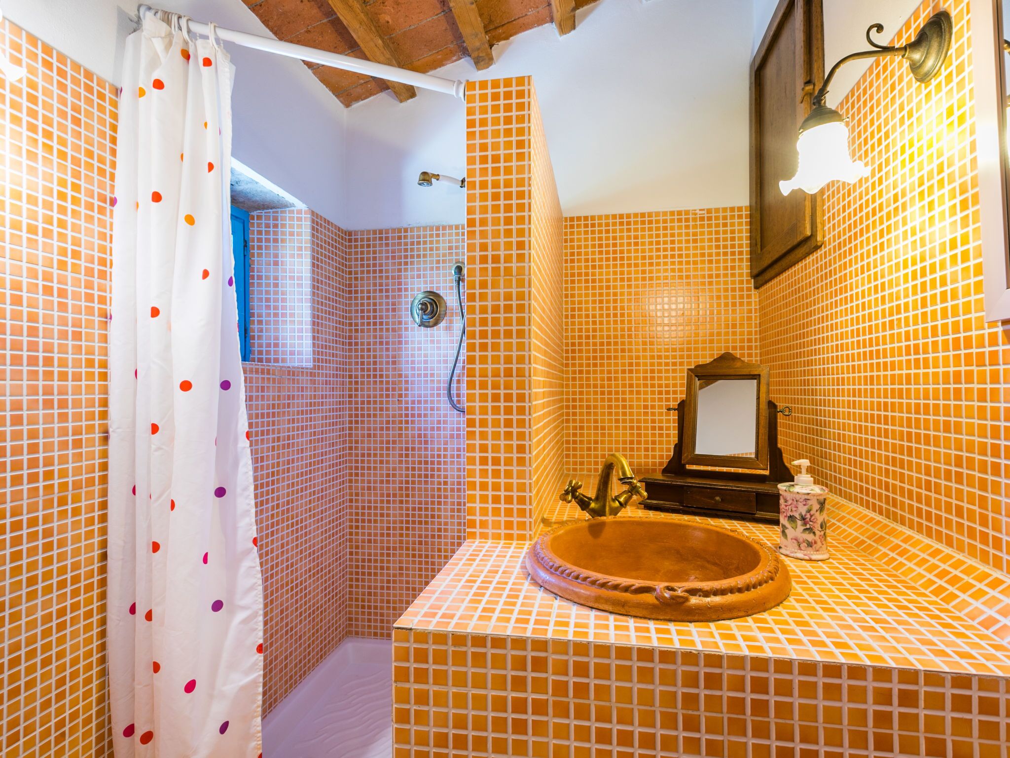 A bathroom with orange tiled walls, a white shower curtain with red polka dots, a wooden sink, and a mirror.