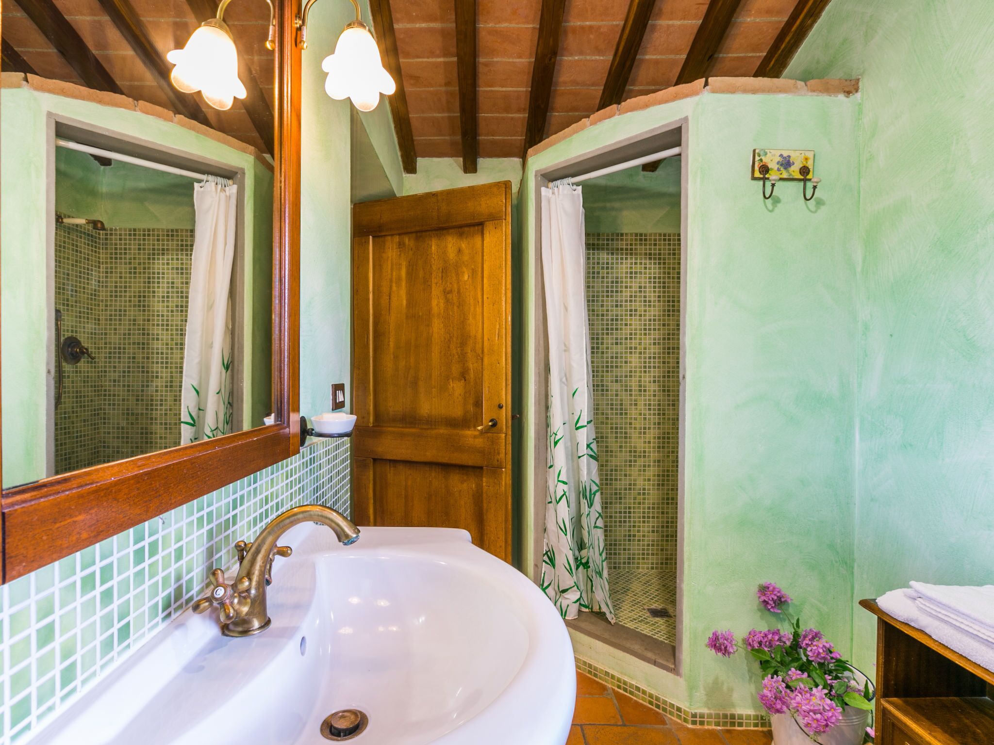 Une salle de bain avec un lavabo blanc, une porte en bois et un espace douche avec un mur vert.