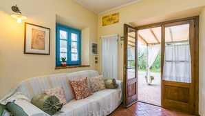 A cozy room with a sofa, a wooden door leading outside, and a small window with blue shutters. - La Casina by Interhome (Vinci)