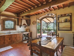 A rustic kitchen with wooden beams, a large window, and a dining area with a table and chairs. - Desideri by Interhome (Vinci)