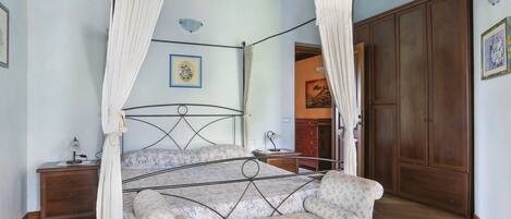 A four-poster canopy bed with a floral-patterned sofa, wooden flooring, and a wooden wardrobe.