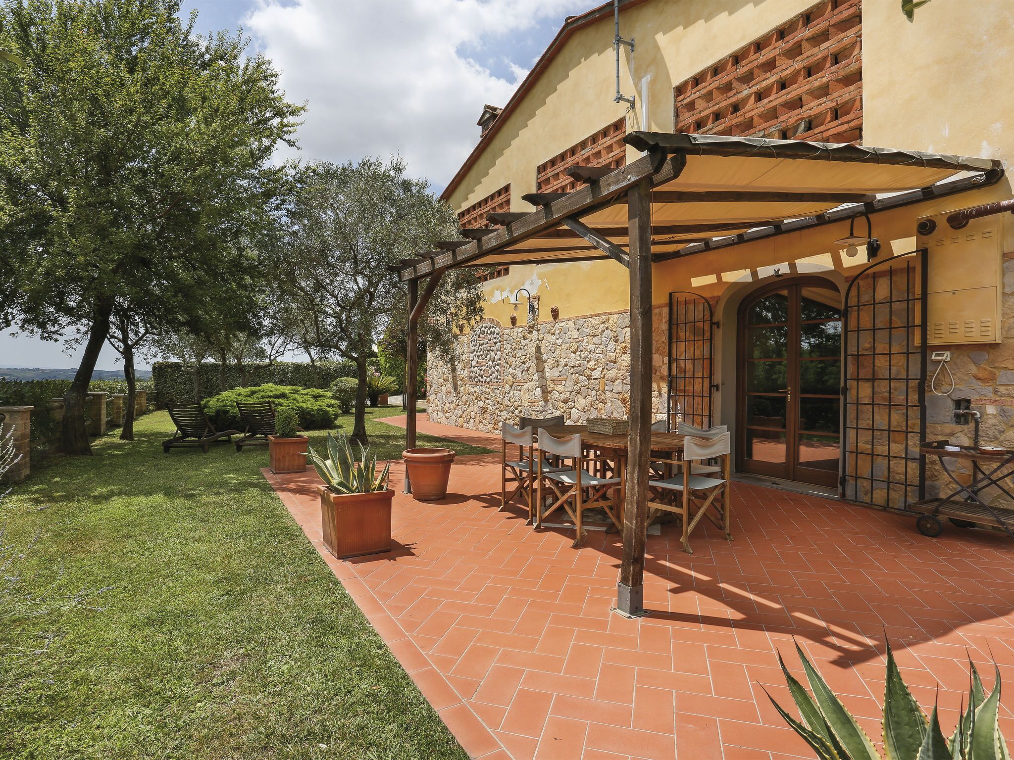 A patio area with a pergola, outdoor seating, and a stone wall.