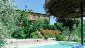 Piscina con sillas de descanso, rodeada de follaje y un edificio de piedra.