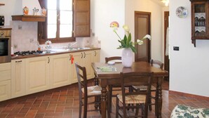 Een keuken met een eethoek, met houten kastjes, een betegelde achterwand en een eettafel met stoelen.