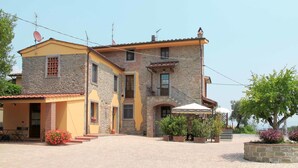 Un edificio de piedra de dos pisos con fachada amarilla, un balcón y un patio empedrado.