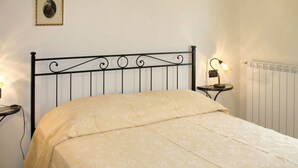 Un dormitorio con cama, una mesita de noche con lámpara, un cuadro enmarcado en la pared y un radiador.