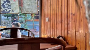 Un intérieur en bois avec une table et des chaises, une fenêtre donnant sur la rue et une enseigne avec des caractères chinois.