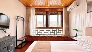 Une chambre avec un plafond en bois, un grand lit, une télévision, une armoire et une fenêtre donnant sur les montagnes.