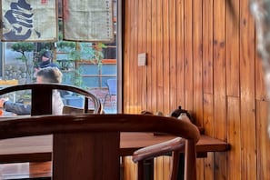 A wooden interior with a table and chairs, a window with a view of the outside, and a wall with a vertical wooden panel. - Lishui Huaxiang. Lisu River View Homestay (Lishui)