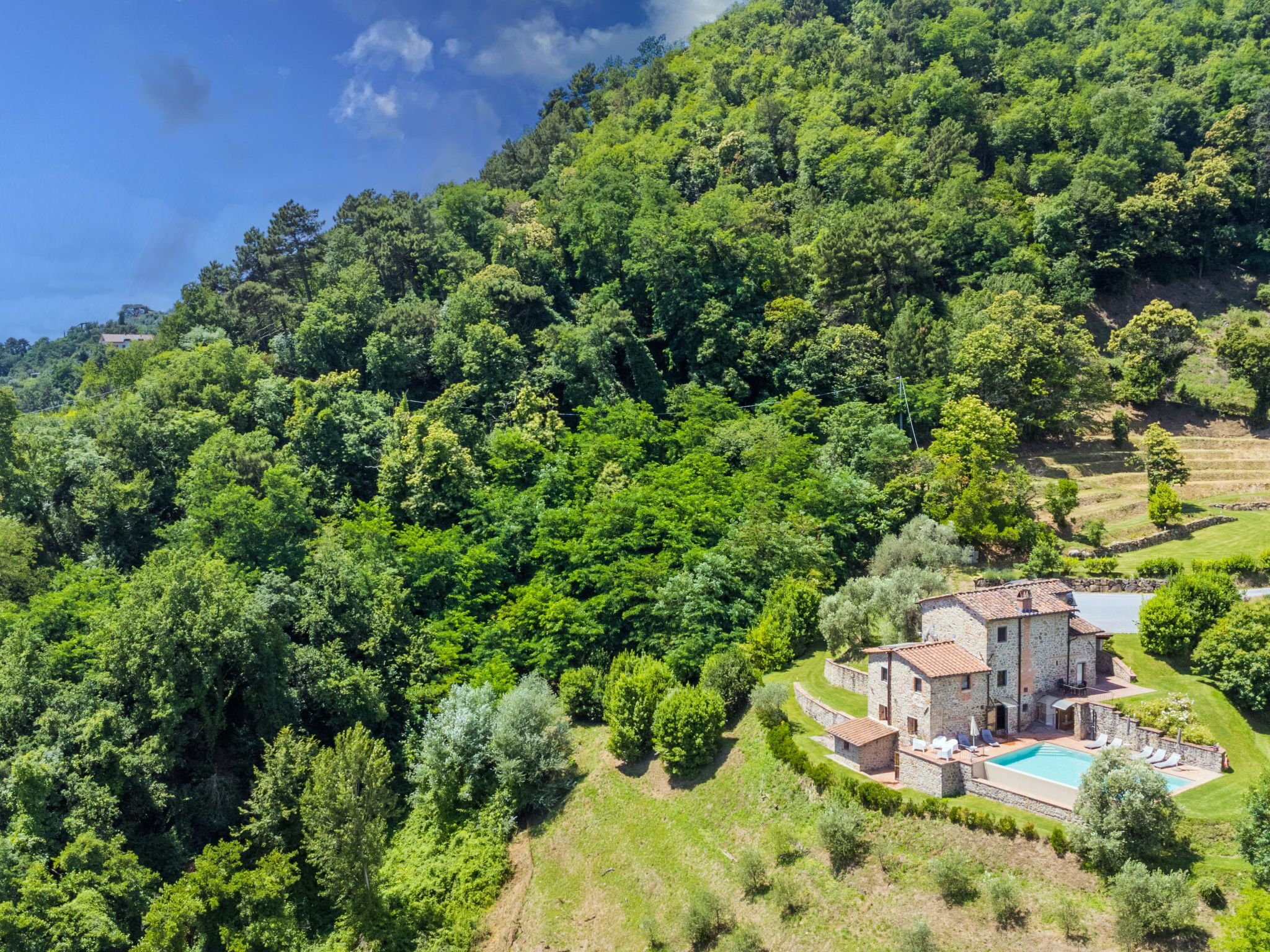 Une maison en pierre dotée d’une piscine, entourée d’une végétation luxuriante et de champs en terrasses.