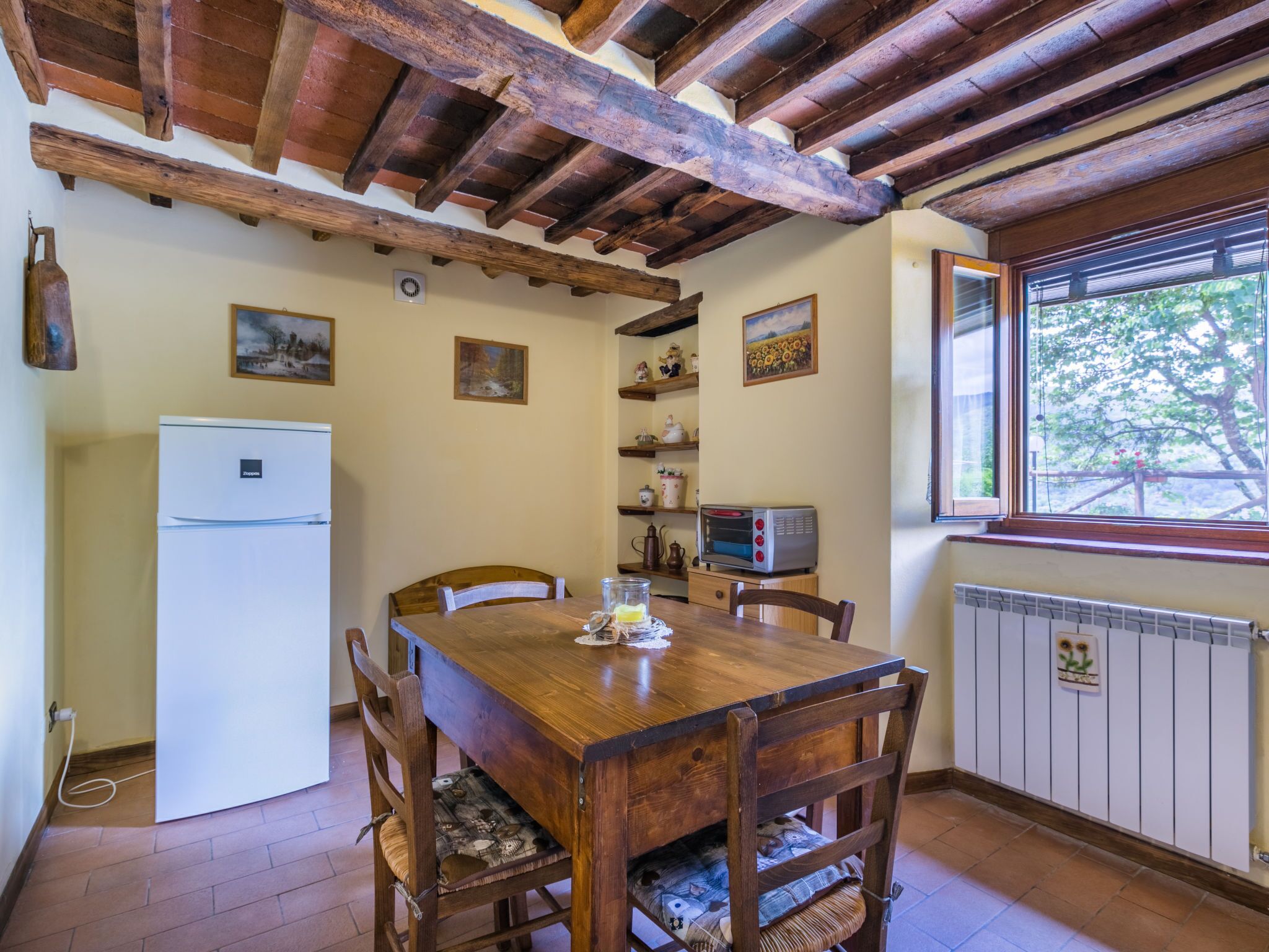 Una cocina rústica con una mesa de madera, sillas, un refrigerador, un microondas y una ventana con vistas a árboles.