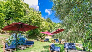 Un espace extérieur aménagé avec des palettes en bois et des coussins bleus, entouré d’une végétation luxuriante et de parasols rouges.