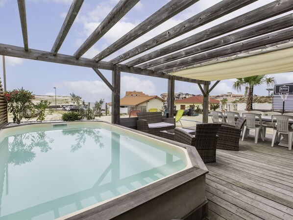 A wooden deck with a hot tub, outdoor seating, and a view of the beach and buildings.